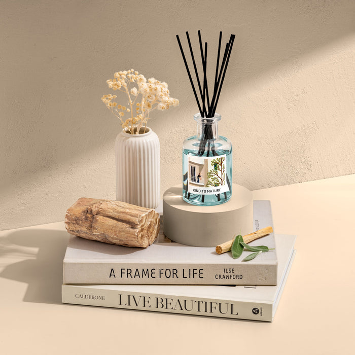 Elle Cadeaux Wood Sage & Sea Salt blue glass reed diffuser styled with driftwood, dried flowers and books in coastal lifestyle setting